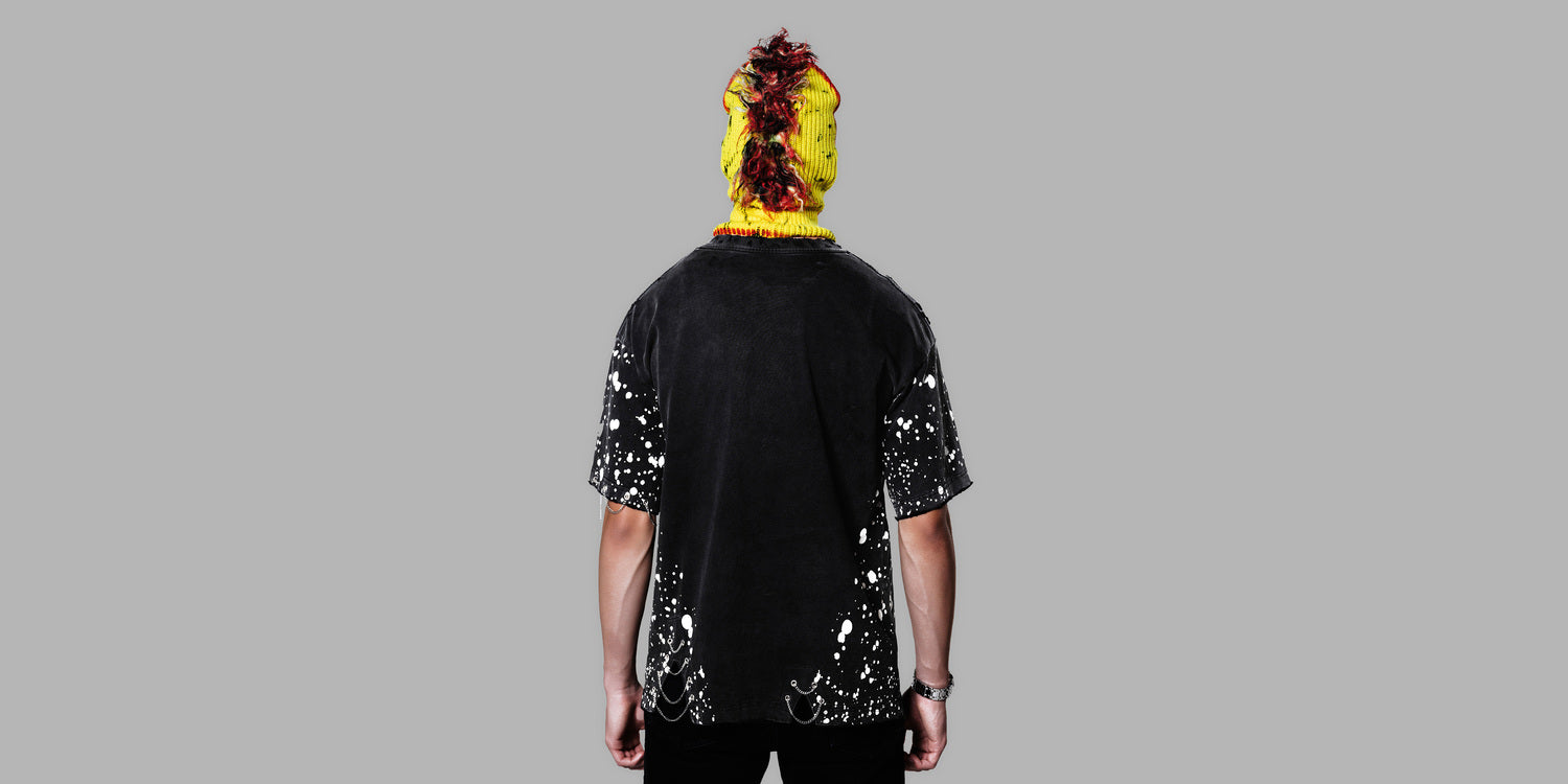 Person wearing a black t-shirt with white splatter design and colorful mask on a gray background