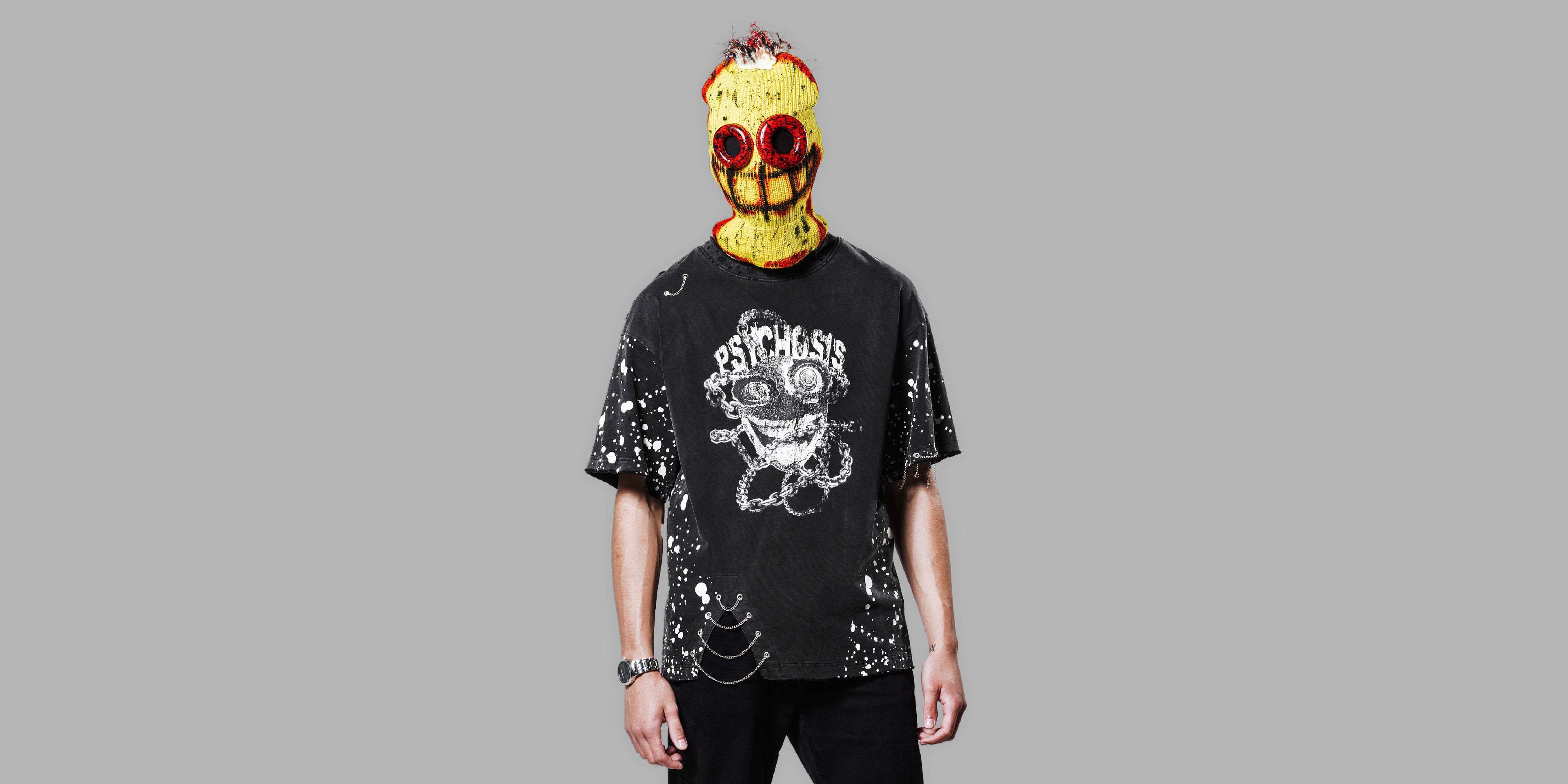 Person wearing a black t-shirt with graphic design and a colorful mask on a gray background